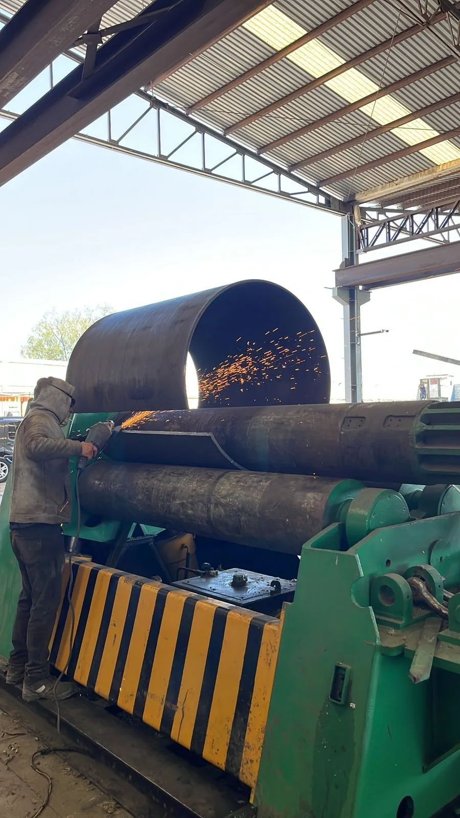 Cuerpo de tanque rolado en la roladora del taller, con el operador cortando el sobrante